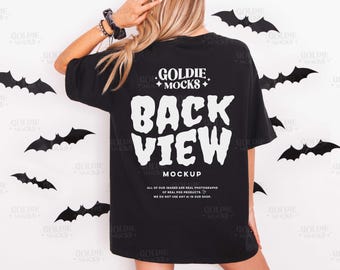 May include: Black t-shirt with the text "BACK VIEW MOCKUP" in white, with the Goldie Mocks logo. The shirt is worn by a person with blonde hair, with black bat decorations on the white background.