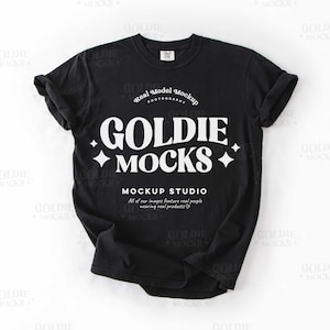 May include: Black t-shirt with white text that reads "Goldie Mocks" and "Mockup Studio". The text is in a retro font style with a star design.