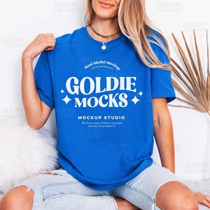 May include: A royal blue t-shirt with the text "GOLDIE MOCKS" in white, featuring a diamond shape on each side. The shirt is short-sleeved and has a round neckline. The words "MOCKUP STUDIO" are below the main text.