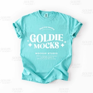 Op de afbeelding: Een turquoise blauwe t-shirt mockup met de tekst "Goldie Mocks" in wit. De tekst is omringd door witte sterren en de woorden "Real Pod Mockup" en "Mockup Studio" zijn ook in wit.