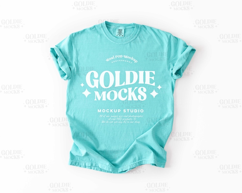 Pode incluir: Uma maquete de camiseta azul turquesa com o texto "Goldie Mocks" em branco. O texto &eacute; cercado por estrelas brancas e as palavras "Real Pod Mockup" e "Mockup Studio" tamb&eacute;m est&atilde;o em branco.