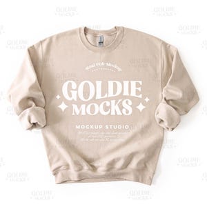 Könnte beinhalten: Ein beigefarbener Sweatshirt-Mockup mit dem Text "Goldie Mocks" und "Mockup Studio" auf der Vorderseite.