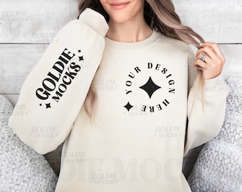 May include: A cream colored sweatshirt with long sleeves and a crew neck. The sweatshirt has a black graphic on the front that says "Your Design Here" with a diamond shape in the center. The sweatshirt also has a black graphic on the left sleeve that says "Goldie Mocks".