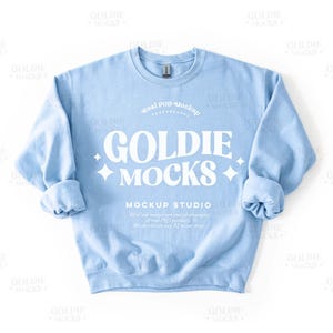 Peut inclure: Un sweat-shirt bleu clair avec le texte "Goldie Mocks Mockup Studio" imprimé sur le devant. Le texte est dans une police blanche rétro.