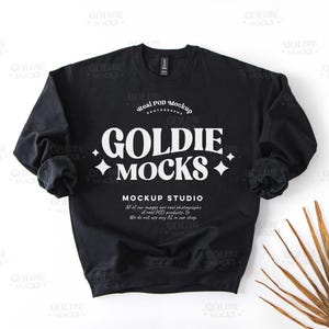 Pode incluir: Mockup de moletom preto com o texto "Goldie Mocks" e "Real POD Mockup Photography" em branco. O texto "Mockup Studio" também está incluído com uma descrição dos serviços da empresa.