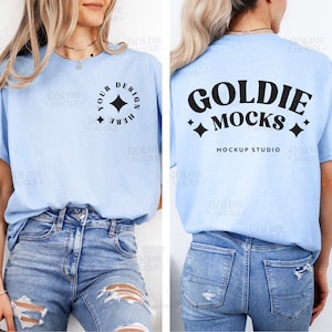 Puede incluir: Una camiseta azul claro con un diseño negro en la parte delantera y el texto "Goldie Mocks Mockup Studio" en la parte posterior. La camiseta está siendo modelada por una persona que lleva pantalones vaqueros azules.