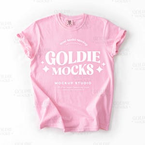 May include: Pink t-shirt mockup featuring the text "GOLDIE MOCKS" and "MOCKUP STUDIO" in white. The text is in a retro font style.