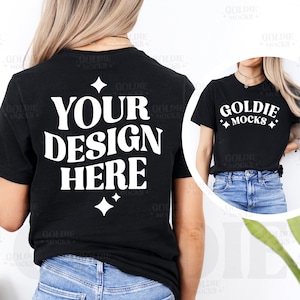 May include: A black t-shirt with the text "YOUR DESIGN HERE" in white. The shirt is being worn by a person with long blonde hair and blue jeans. The text "GOLDIE MOCKS" is also visible on the shirt.