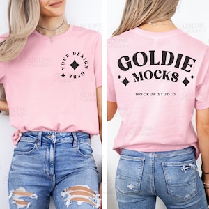 Puede incluir: Una camiseta rosa claro con el texto "YOUR DESIGN HERE" en un círculo en la parte delantera y "GOLDIE MOCKS" en la parte trasera. La camiseta se combina con unos vaqueros azules.