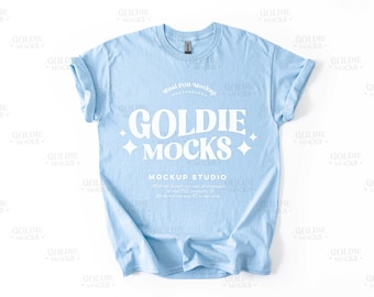 Könnte beinhalten: Ein hellblaues T-Shirt mit dem Text "Goldie Mocks" in Weiß. Der Text ist in einem Retro-Schriftart-Stil gehalten und von weißen Sternen umgeben. Die Texte "Real POD Mockup" und "Mockup Studio" sind ebenfalls in Weiß sichtbar.