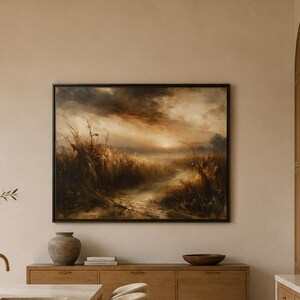 May include: A kitchen interior featuring a large marble island with a sink and faucet, a beige vase with greenery, and upholstered stools. A landscape painting hangs on the wall above a wooden sideboard, with a range stove and wooden cabinetry.
