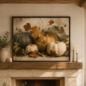May include: A framed wall art print depicting a collection of pumpkins and autumn leaves in shades of orange, white, and dark green. The artwork is displayed above a stone fireplace mantel in a living room with two armchairs and a coffee table.
