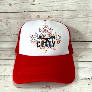May include: Red and white trucker hat with a white maple leaf design. The maple leaf is filled with colourful dots and the text "Dangle Snipe Celly" is printed on the leaf.