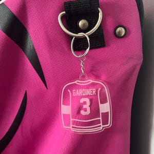 May include: A white acrylic keychain shaped like a hockey jersey with the name "GARDINER" and the number "3" printed on it.
