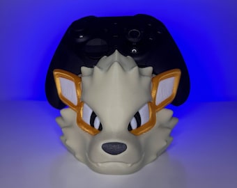 May include: A cream-colored, 3D-printed wolf head with gold and white accents, designed to hold a black game controller. The controller rests on top of the wolf's head, creating a unique display for gaming accessories.