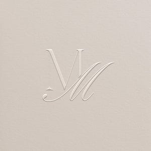Puede incluir: Un fondo color crema con un monograma en relieve con las letras "M" y "M" en una escritura delicada y elegante. El diseño es minimalista y sofisticado, con una textura sutil.