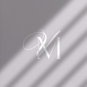 May include: Elegant white monogram logo featuring the intertwined letters 'M' and 'V' on a textured gray background. The design includes a flowing script element, with shadows adding depth. The overall aesthetic is minimalist and sophisticated.