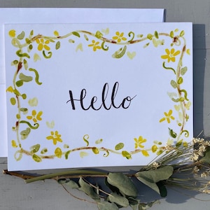 May include: A white card with a yellow floral border and the word "Hello" written in black ink.