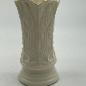 May include: A white ceramic vase with a gold rim and intricate floral designs. The vase has a scalloped top and a wide base.