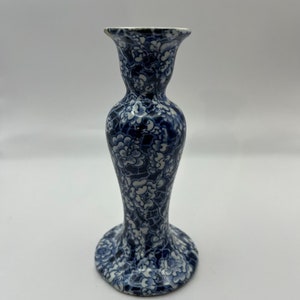 May include: A blue and white ceramic candle holder with a floral pattern. The holder has a wide base and a narrow neck.