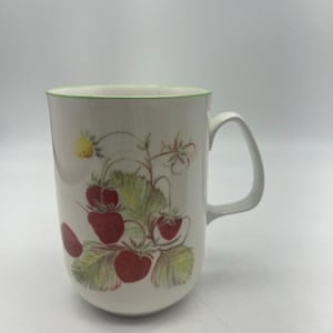 May include: A white ceramic mug with a green rim and a floral design featuring red strawberries and green leaves.