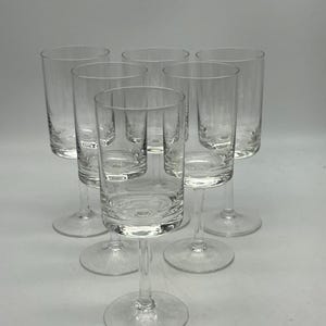 May include: Set of six clear glass shot glasses with a simple design. The glasses have a straight, cylindrical shape with a short stem and a round base.
