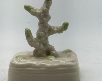 Op de afbeelding: Een keramische koraalsculptuur in beige en groene tinten. Het koraal staat op een rechthoekige basis met een getextureerd oppervlak, dat een zeegezicht oproept. De uiteinden van de koraaltakken zijn lichtgroen.
