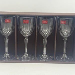 May include: Set of four clear crystal wine glasses with a diamond pattern. The glasses are in a brown box with the words "Crystal D'arques" on the label.