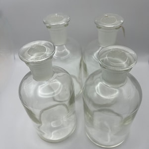 Peut inclure: Quatre bouteilles en verre transparent avec des bouchons en verre. Les bouteilles sont vides et ont une forme ronde.