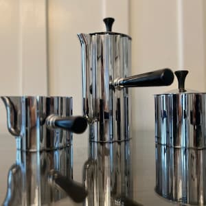 May include: A silver coffee and tea set with black handles. The set includes a coffee pot, creamer, and sugar bowl. Each piece has a vertical ribbed design.