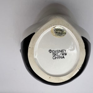 Peut inclure: Une tasse en c&eacute;ramique noire et blanche avec un logo Disney au fond. Le logo indique "Disney SKL/WW China".