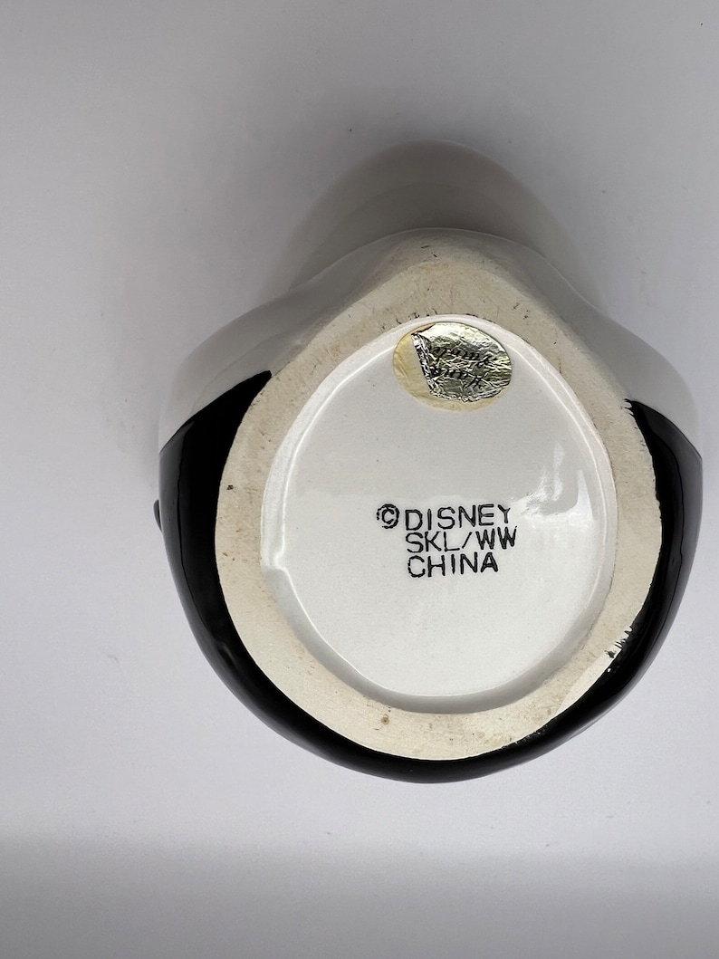 Peut inclure: Une tasse en c&eacute;ramique noire et blanche avec un logo Disney au fond. Le logo indique "Disney SKL/WW China".