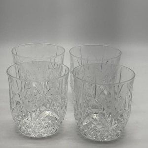 Op de afbeelding: Vier heldere, geslepen glazen bekers. Elk glas heeft een gedetailleerd, getextureerd patroon van verticale en ruitvormen. De glazen zijn cilindrisch met een licht afgeronde basis.