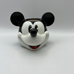 Peut inclure: Pot en c&eacute;ramique noir et blanc en forme de t&ecirc;te de Mickey Mouse. Le pot a un nez noir, des oreilles noires et une bouche rouge.