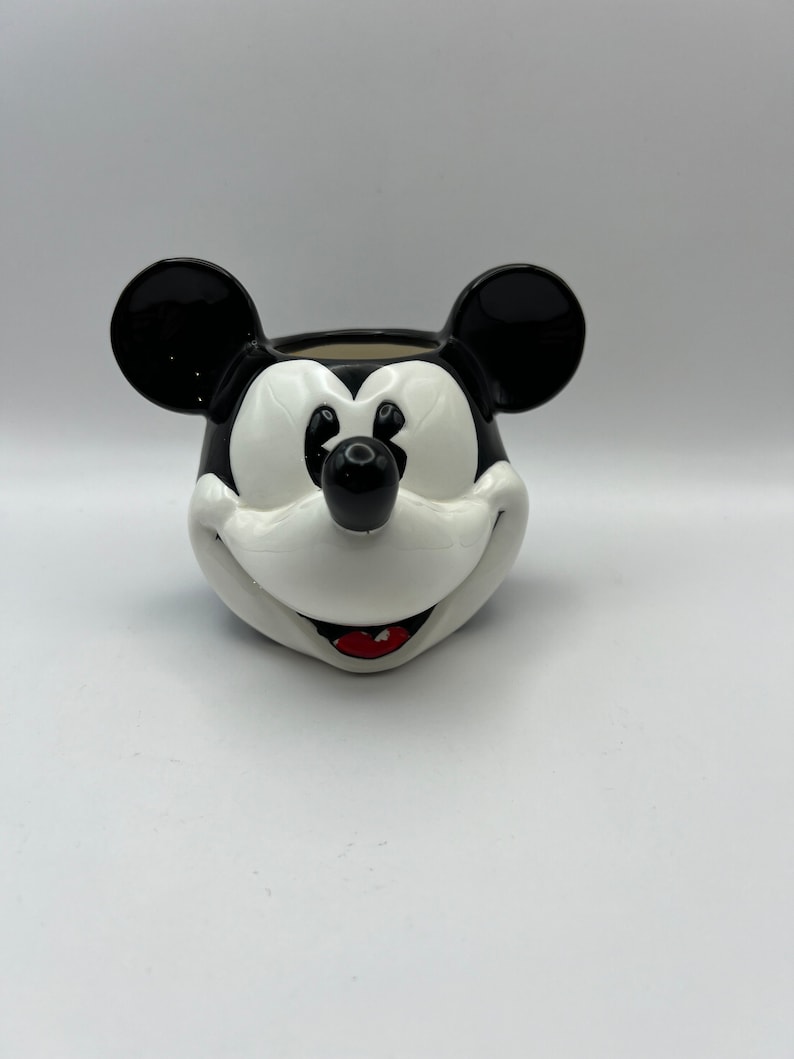 Peut inclure: Pot en c&eacute;ramique noir et blanc en forme de t&ecirc;te de Mickey Mouse. Le pot a un nez noir, des oreilles noires et une bouche rouge.