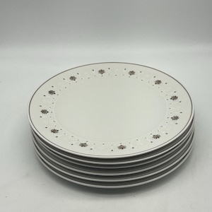 Op de afbeelding: Een stapel van zes witte keramische dinerborden met een gouden en wit bloemmotief rond de rand.