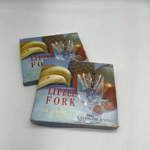 Puede incluir: Dos cajas de tenedores de acero inoxidable Little Fork. Las cajas son azules y blancas con una imagen de fruta y tenedores. El texto en la caja dice "Little Fork 12 pcs. set Stainless Steel."