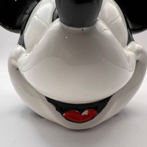 Peut inclure: Une figurine en c&eacute;ramique blanche repr&eacute;sentant la t&ecirc;te de Mickey Mouse avec des oreilles noires et une bouche rouge. La figurine est une repr&eacute;sentation classique du personnage embl&eacute;matique de Disney.