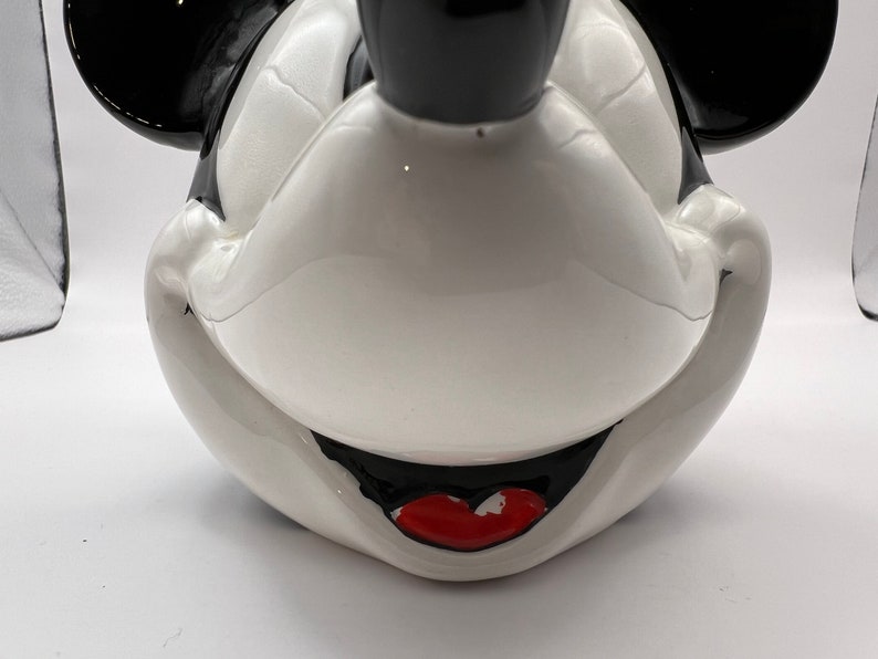 Peut inclure: Une figurine en c&eacute;ramique blanche repr&eacute;sentant la t&ecirc;te de Mickey Mouse avec des oreilles noires et une bouche rouge. La figurine est une repr&eacute;sentation classique du personnage embl&eacute;matique de Disney.