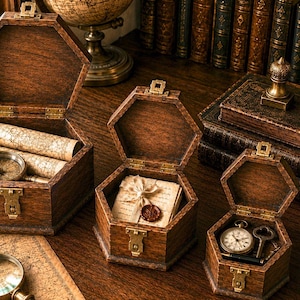 Puede incluir: Tres cajas hexagonales de madera de color marrón oscuro con cierres y bisagras de latón. La caja más grande contiene mapas enrollados y una brújula. La caja mediana contiene una carta con un sello de cera. La caja más pequeña contiene un reloj.
