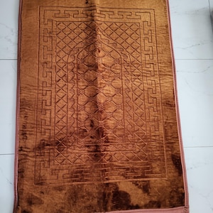 May include: A brown prayer rug with a geometric pattern and a fringed border. The rug has a central arch design.