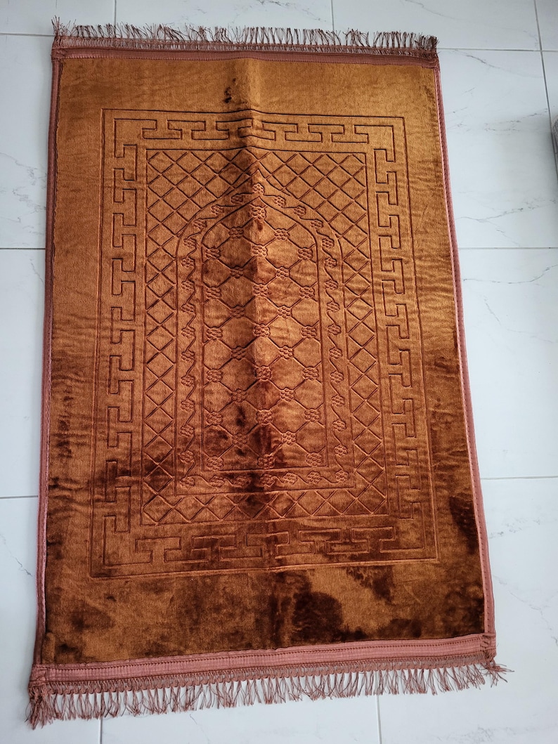 May include: A brown prayer rug with a geometric pattern and a fringed border. The rug has a central arch design.