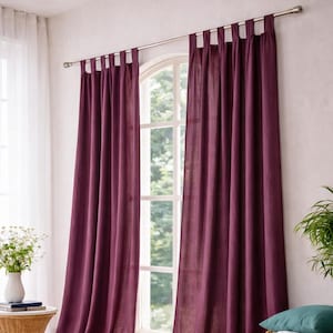 May include: Burgundy-colored linen curtains hanging from a silver rod. The curtains are draped and cover a large window. A small table with a vase of flowers and a woven basket are in the foreground.