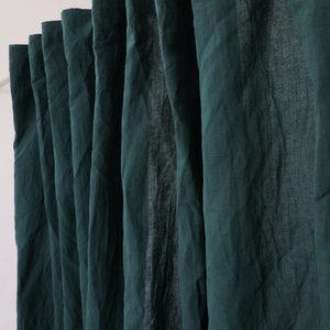 May include: A set of dark green linen curtains hanging in a window. The curtains are gathered at the top and have a natural, relaxed look.