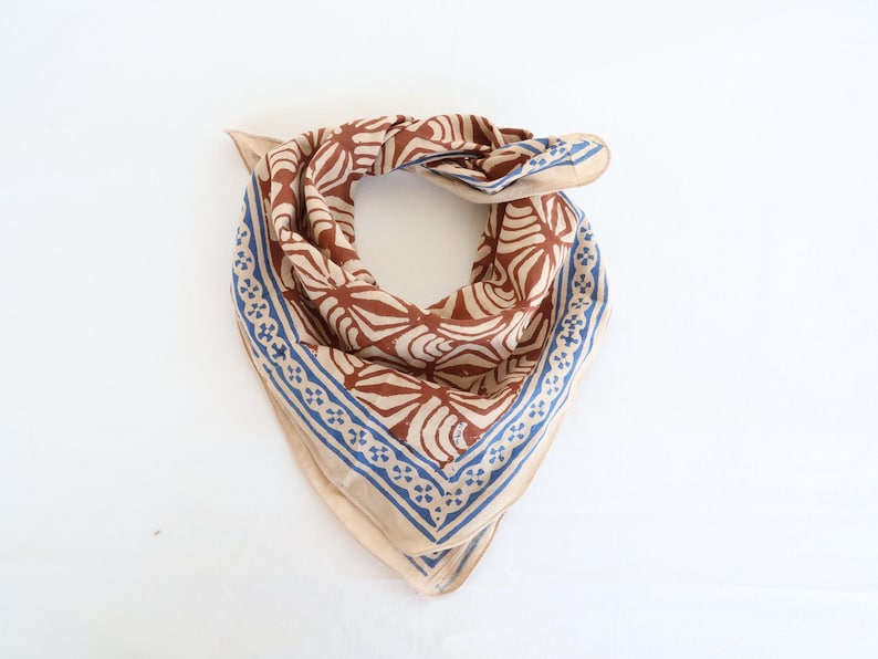 Może przedstawiać: Brązowo-beżowa bandana z niebieskim wzorem kwiatowym. Bandana ma geometryczny wz&oacute;r z niebiesko-białą obw&oacute;dką.
