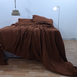 May include: A brown linen duvet cover with a relaxed, rumpled look. The duvet cover is on a bed with two pillows, one brown and one white.