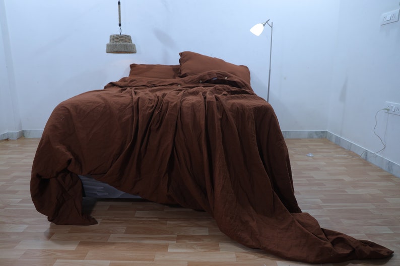 May include: A brown linen duvet cover with a relaxed, rumpled look. The duvet cover is on a bed with two pillows, one brown and one white.