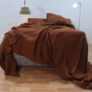 May include: A brown linen duvet cover with a crumpled look, draped over a bed with two matching pillowcases. The duvet cover is made of a soft, natural fabric and has a relaxed, casual look.
