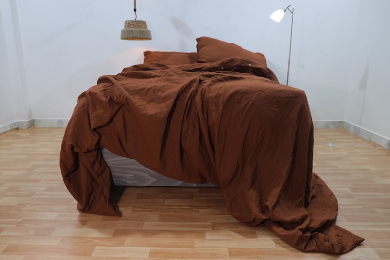 May include: A brown linen duvet cover with a crumpled look, draped over a bed with two matching pillowcases. The duvet cover is made of a soft, natural fabric and has a relaxed, casual look.