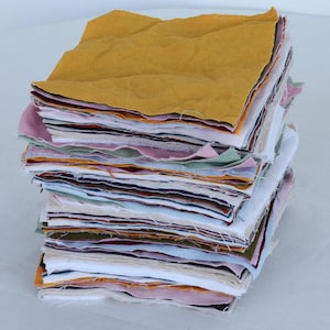 May include: A stack of fabric squares in various colors, including yellow, pink, green, and white. The squares are stacked neatly and are ready for a quilting project.